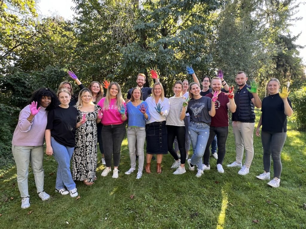 Teambuilding und REC-Workshop: Das gesamte Team hat sich die Hände bunt gemacht und steht im Grünen
 